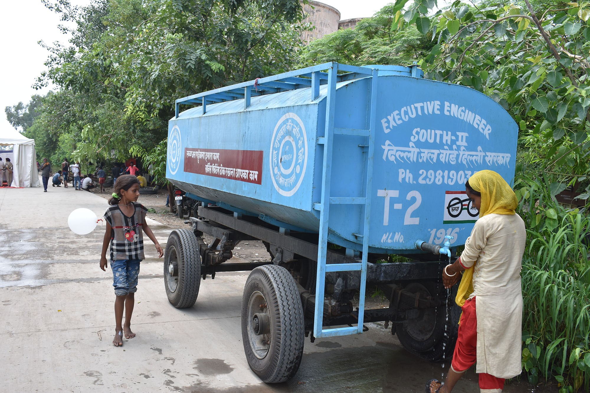 A woman draws drinking water from a water tanker provided by Delhi Jal Board (the city's water supply agency) at a makeshift relief camp during the Yamuna flood in 2019, India